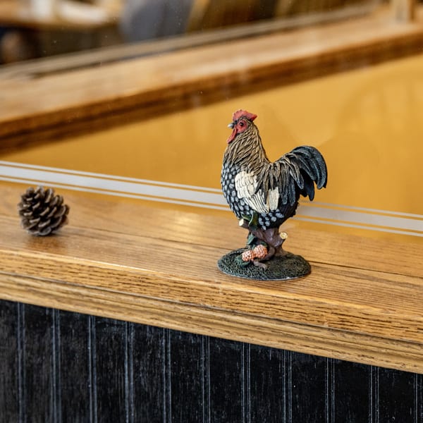 A decorative rooster figurine and a pinecone sit on a wooden ledge at Chicken Run.