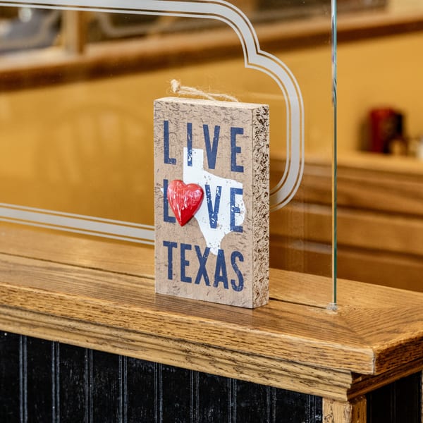A wooden sign with "Live Love Texas" and a red heart, on a counter at Chicken Run.