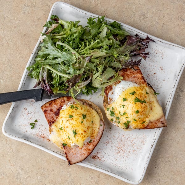 Two Eggs Benedict with hollandaise sauce and a side salad on a white rectangular plate.