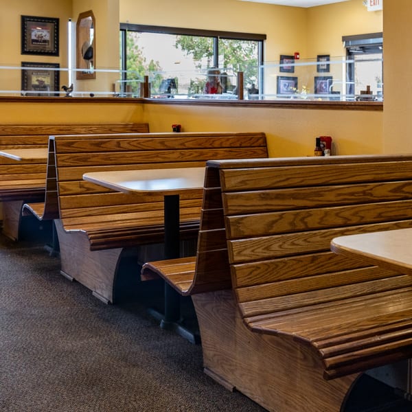 Empty wooden booths and tables in a brightly lit Chicken Run restaurant dining area.