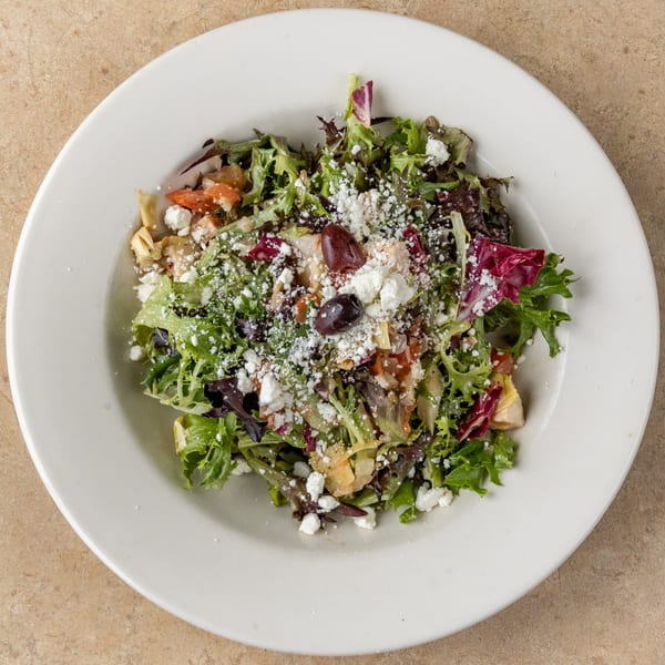A fresh green salad with feta cheese, olives, and chicken on a white plate.