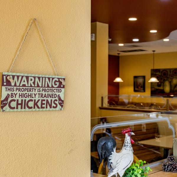 A "Warning: This property is protected by highly trained chickens" sign hangs on a yellow wall.