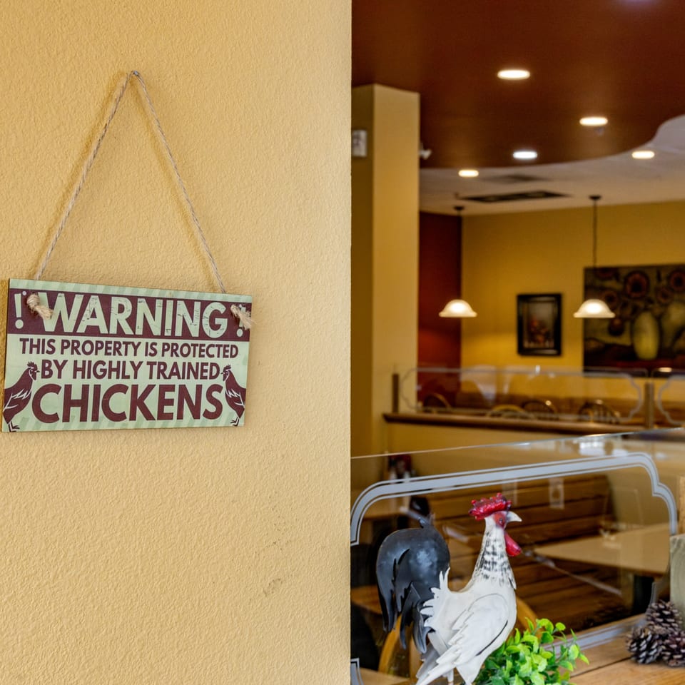 A "Warning: This property is protected by highly trained chickens" sign hangs on a yellow wall.