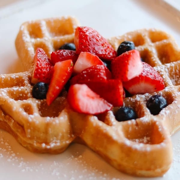 Golden waffles topped with fresh strawberries, blueberries, and powdered sugar on a white plate.