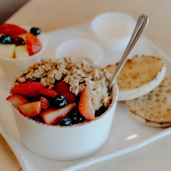 A white bowl of yogurt with granola, strawberries, and blueberries, next to English muffins.