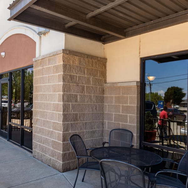 Outdoor patio seating with black metal tables and chairs outside Chicken Run, reflecting cars and a person.