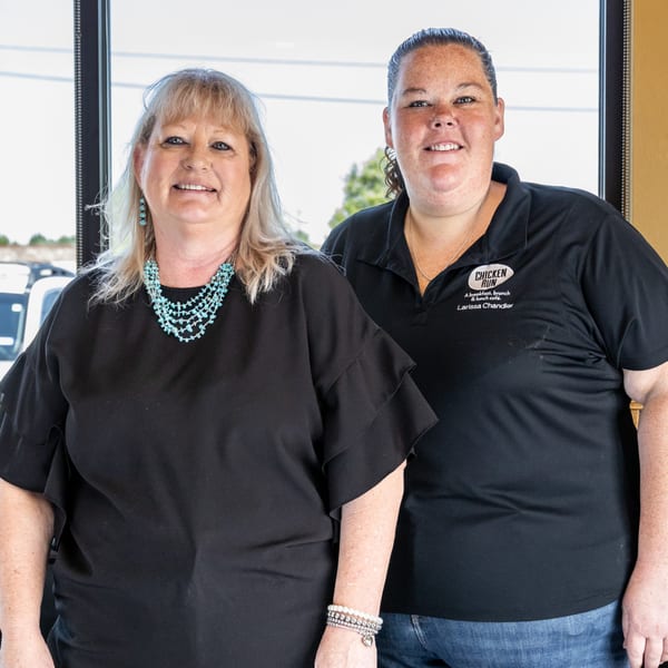 Two women, one in a black top and turquoise necklace, the other in a Chicken Run polo.